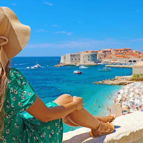 en tjej med stråhatt sitter på utsiktspunkt och tittar utöver Dubrovnik