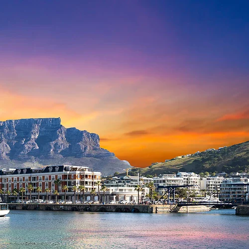 En bild av Kapstads hamn vid solnedgång med Table Mountain i bakgrunden, där den färgglada himlen reflekteras i vattnet. Perfekt för att visa Sydafrikas natursköna stad och hamn.